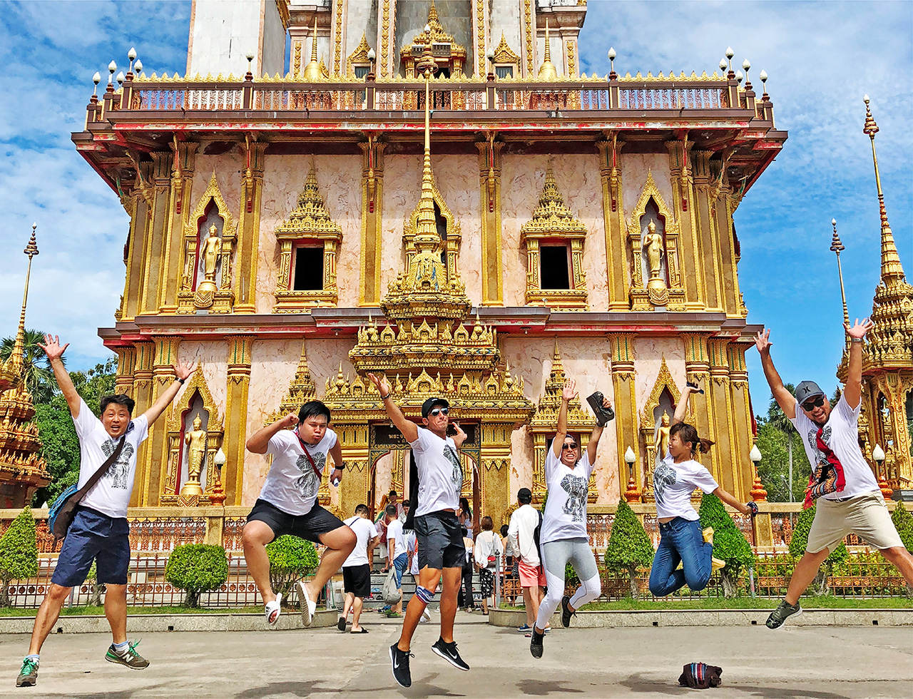 A team of people doing a jump shot group photo in front of an iconic temple in Phuket
